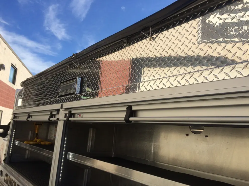 Exterior view of small fire truck showing cab, body compartments, and wheel/tire area.
