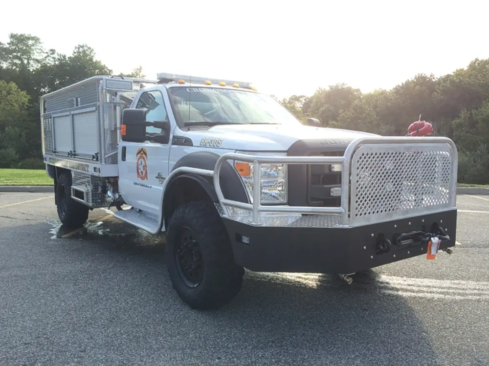 Exterior view of small fire truck showing cab, body compartments, and wheel/tire area.