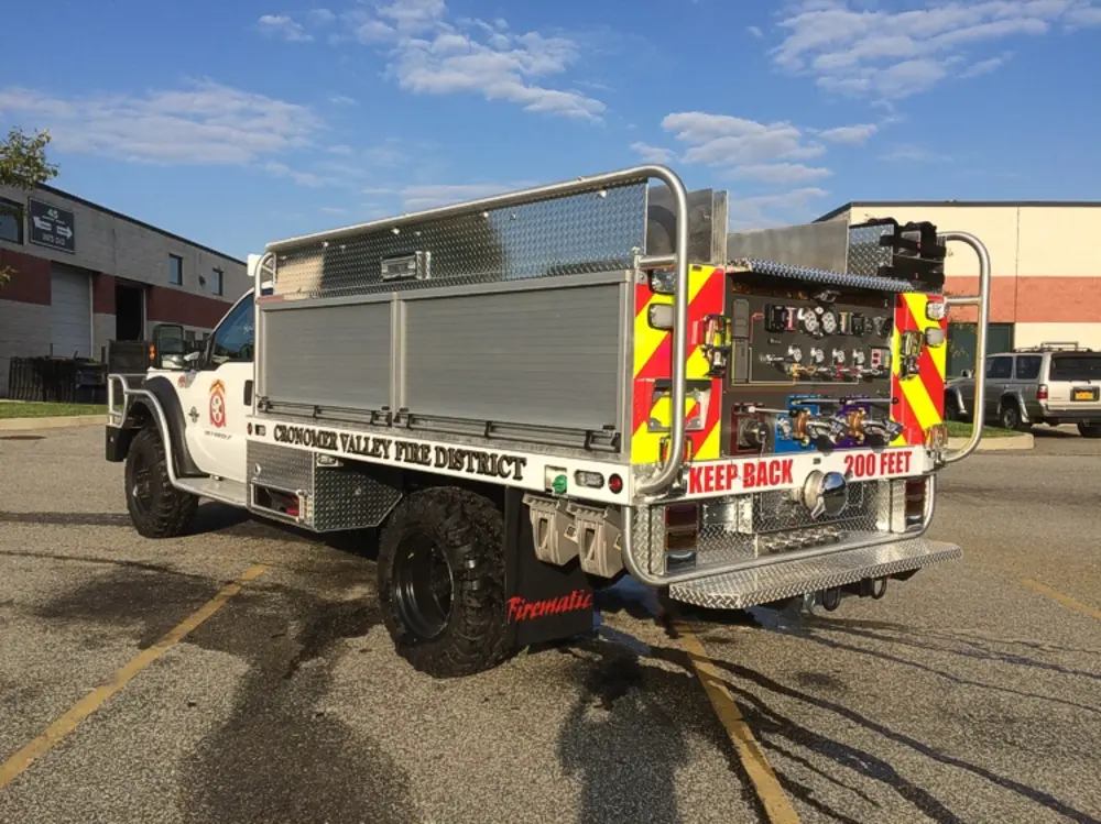 Exterior view of small fire truck showing cab, body compartments, and wheel/tire area.