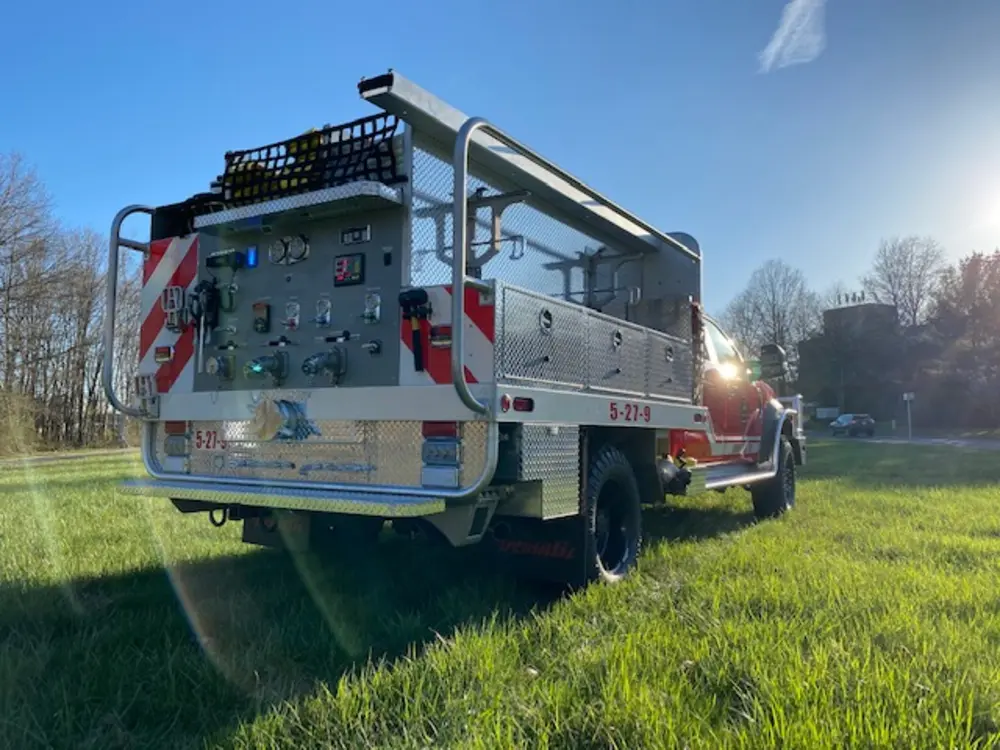 Exterior view of small fire truck showing cab, body compartments, and wheel/tire area.