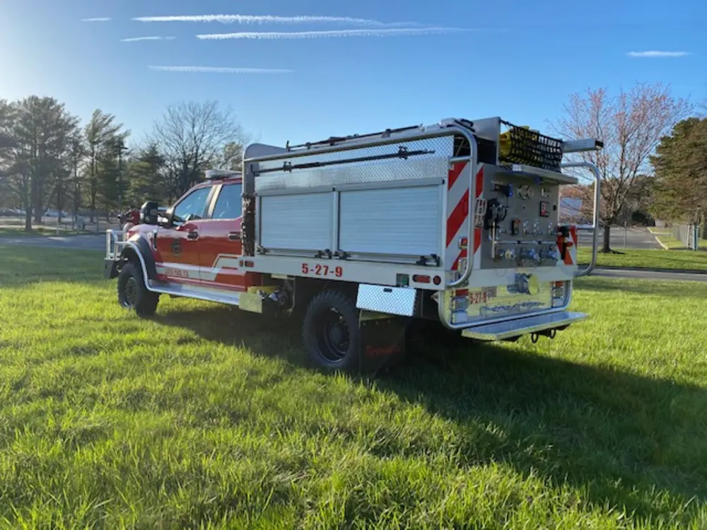 Exterior view of small fire truck showing cab, body compartments, and wheel/tire area.