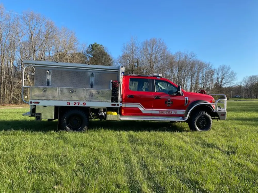 Exterior view of small fire truck showing cab, body compartments, and wheel/tire area.
