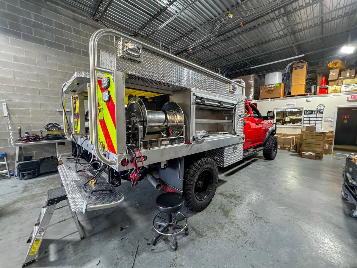 Left-side rear body view showing the open shelf compartment, hose reel bay, and wheel area.