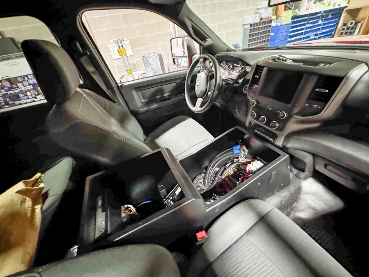 Cab interior view showing front seats, dashboard controls, steering wheel, and open center console wiring.