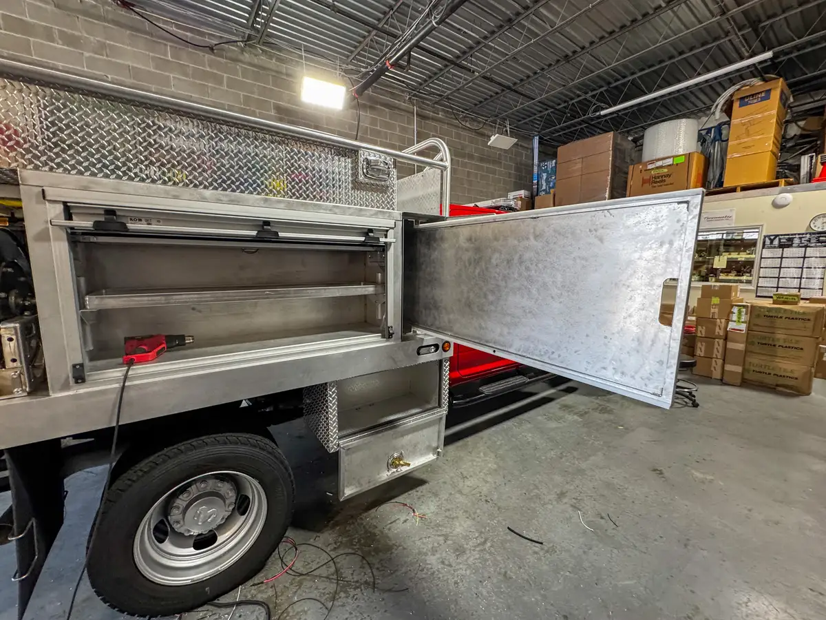 Another left-side angle of the open long compartment door and shelf bay on the utility body.