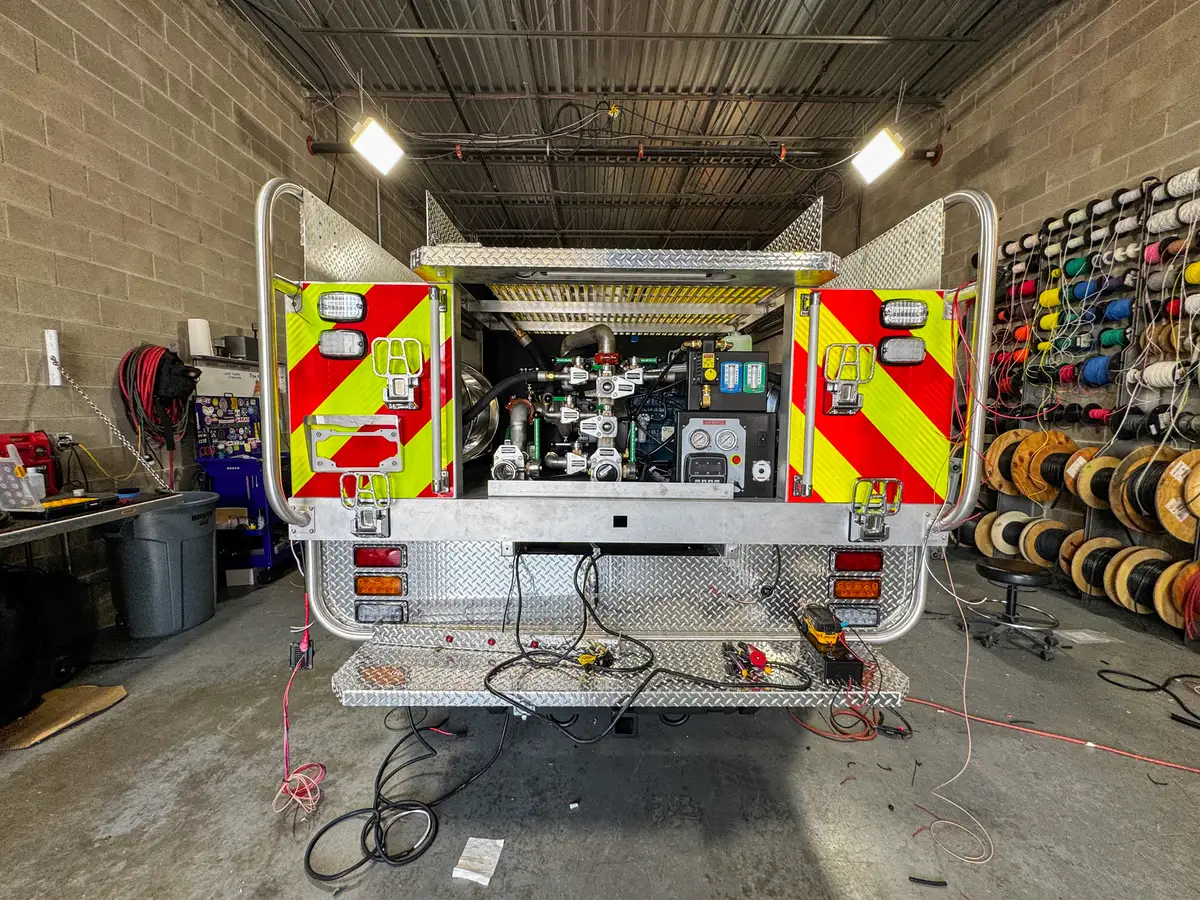 Centered rear view with open doors showing pump panel controls, gauges, and hose connections.