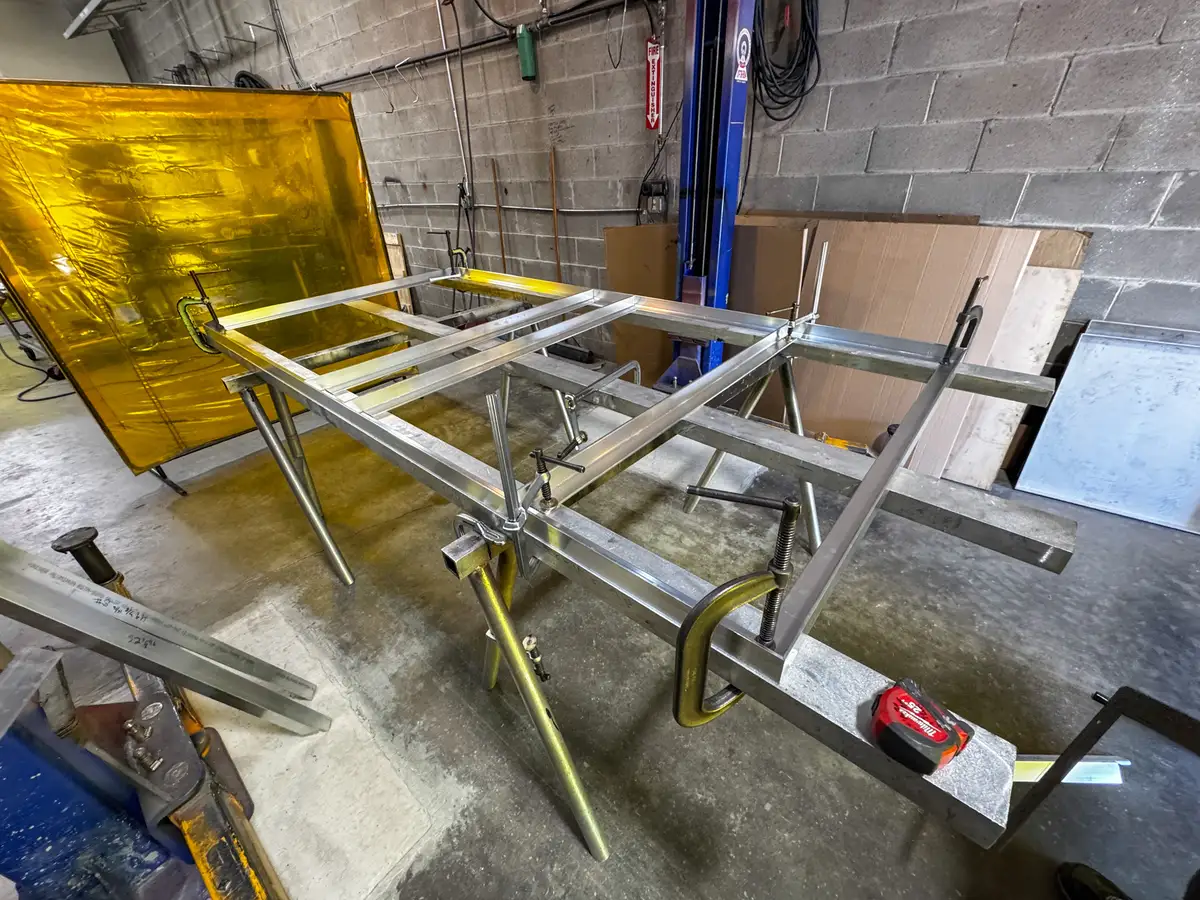 Fabrication-stage body frame on stands showing compartment framing and clamps in the shop.