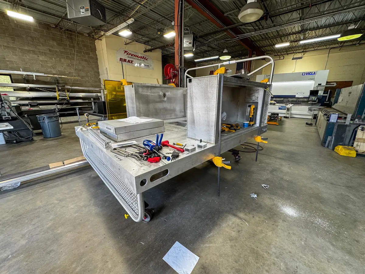 Utility body module on the shop floor with open compartments and tools laid out on the deck.