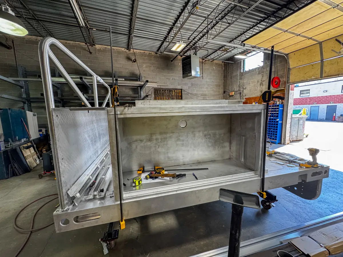 Side compartment view of the unfinished body module showing open storage bay and tools inside.