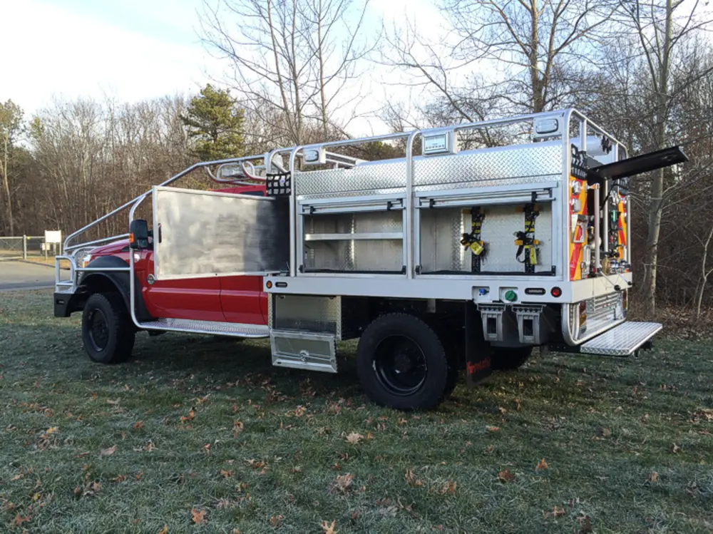 Exterior view of small fire truck showing cab, body compartments, and wheel/tire area.