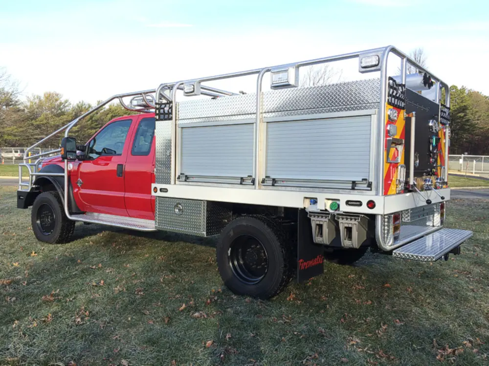 Exterior view of small fire truck showing cab, body compartments, and wheel/tire area.
