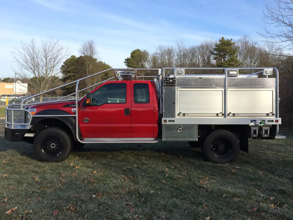 Exterior view of small fire truck showing cab, body compartments, and wheel/tire area.