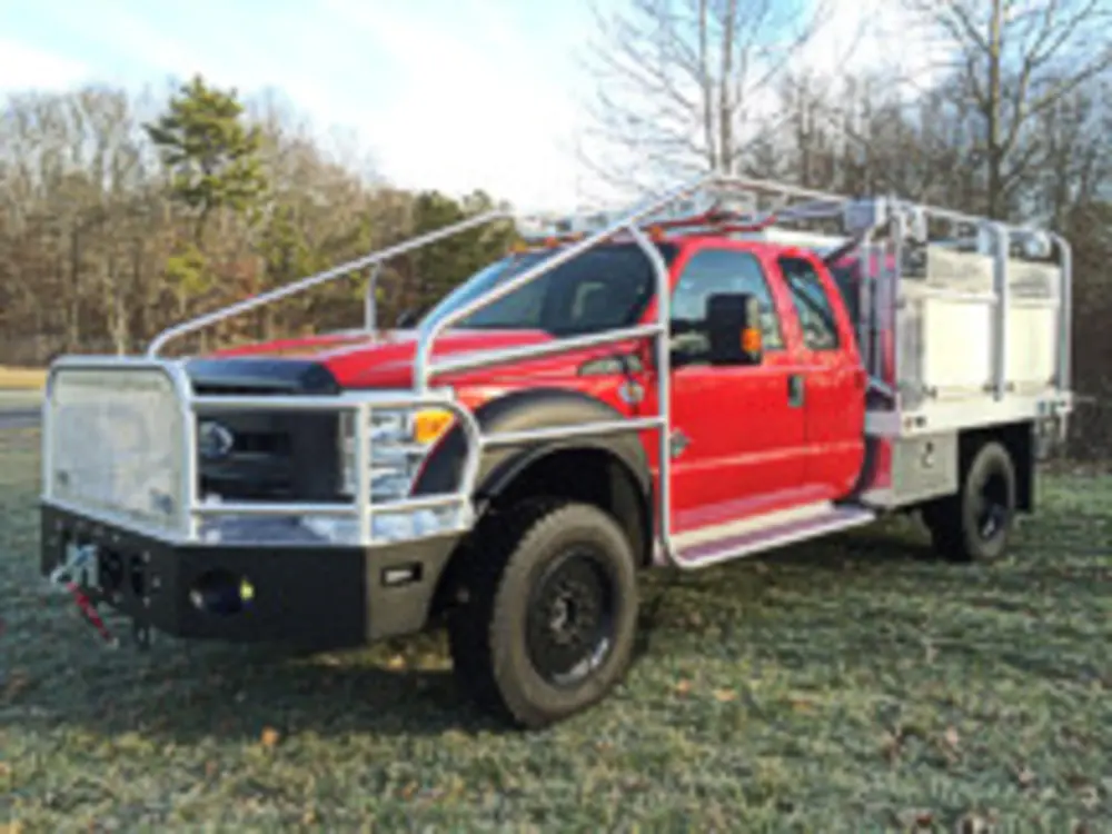 Exterior view of small fire truck showing cab, body compartments, and wheel/tire area.