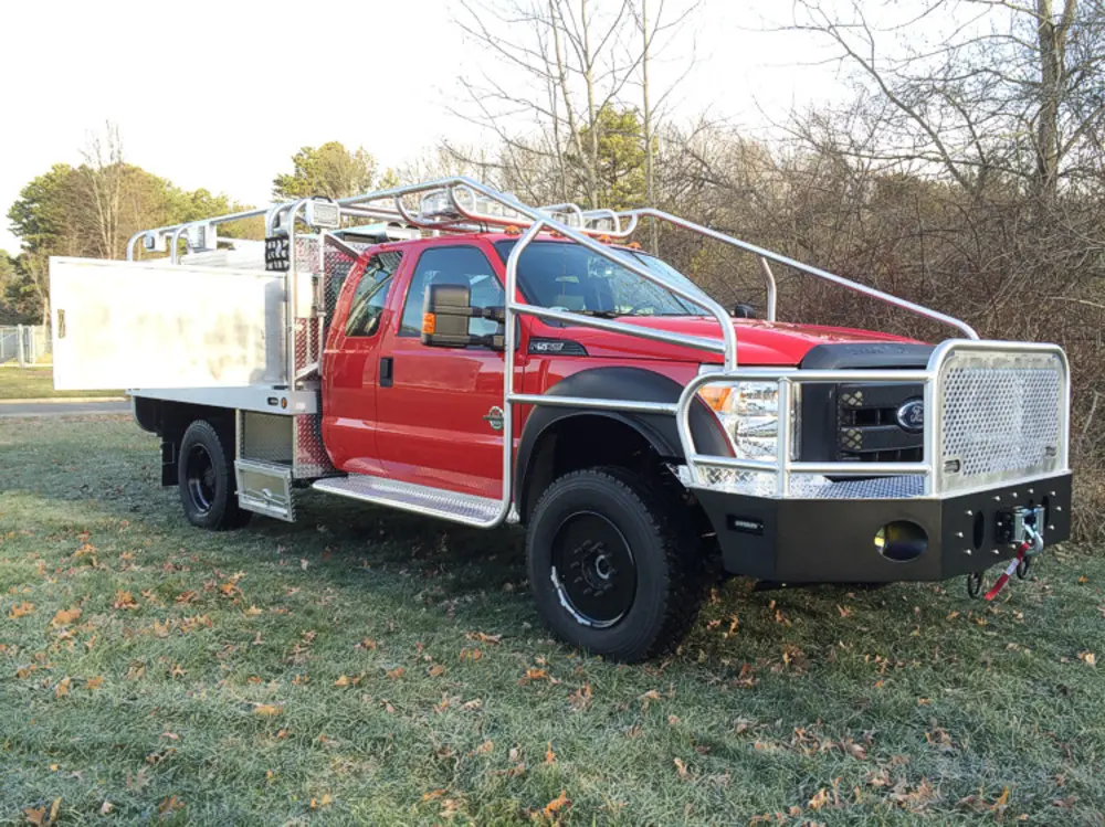 Exterior view of small fire truck showing cab, body compartments, and wheel/tire area.
