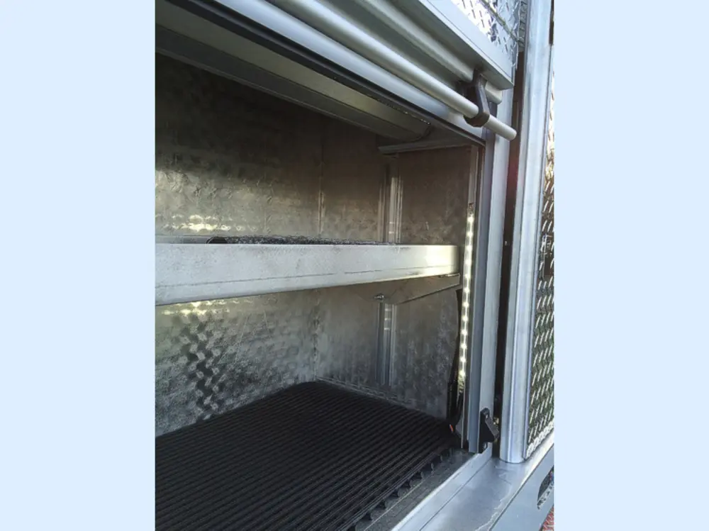 Exterior view of small fire truck showing cab, body compartments, and wheel/tire area.