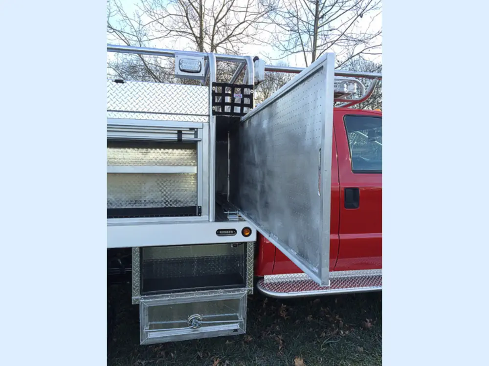 Exterior view of small fire truck showing cab, body compartments, and wheel/tire area.