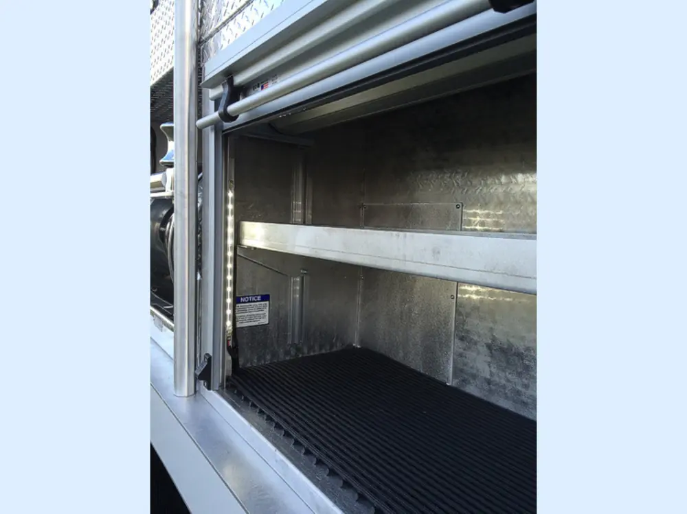 Exterior view of small fire truck showing cab, body compartments, and wheel/tire area.