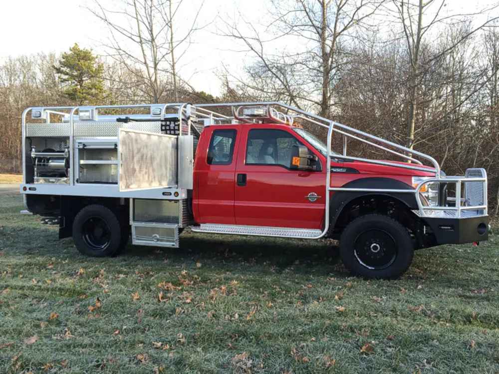 Exterior view of small fire truck showing cab, body compartments, and wheel/tire area.