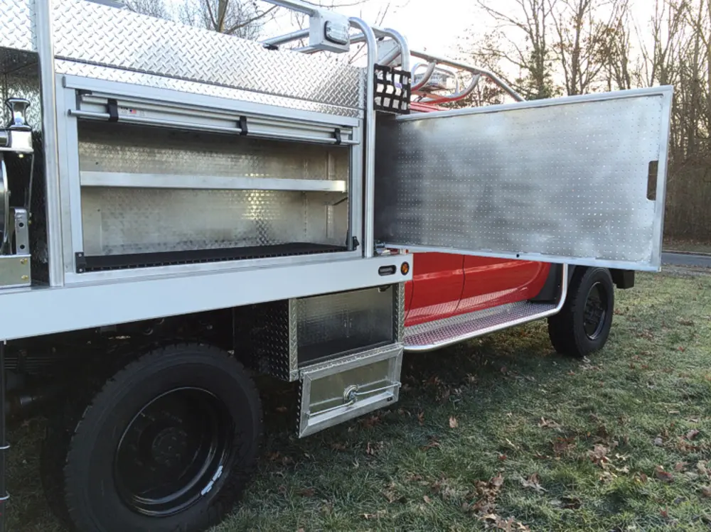 Exterior view of small fire truck showing cab, body compartments, and wheel/tire area.