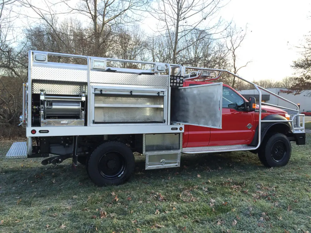 Exterior view of small fire truck showing cab, body compartments, and wheel/tire area.