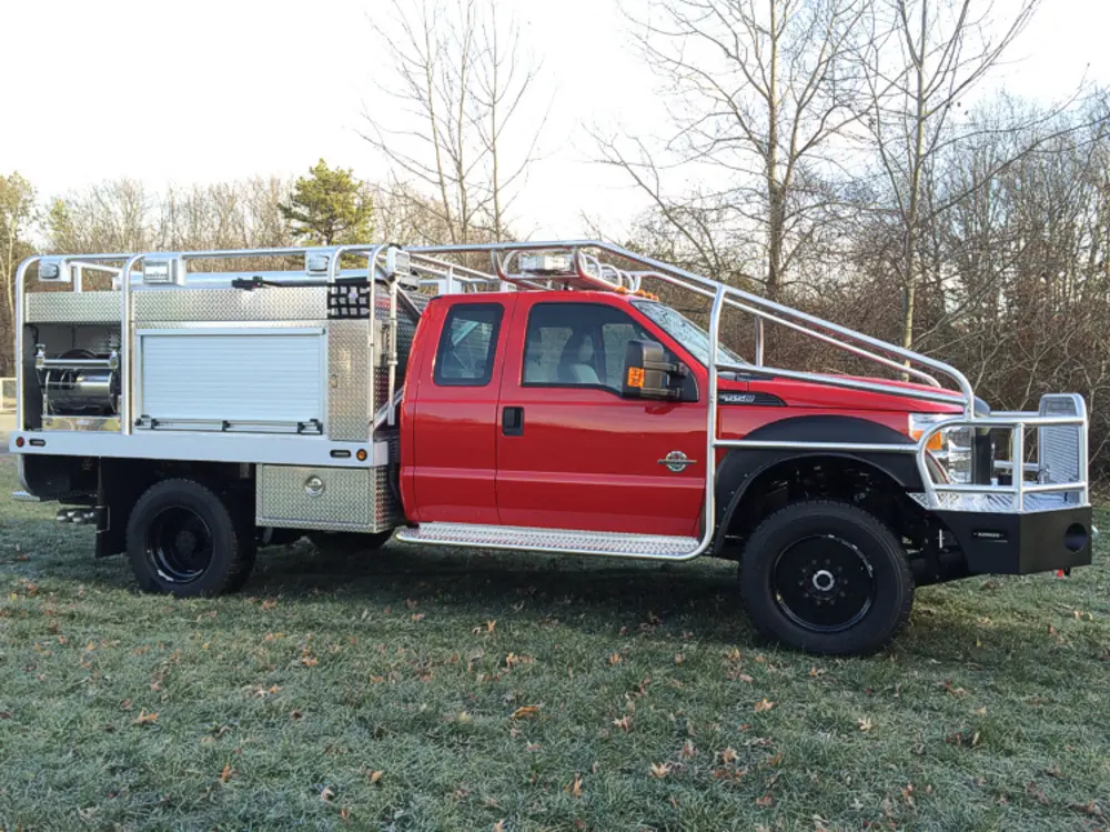 Exterior view of small fire truck showing cab, body compartments, and wheel/tire area.