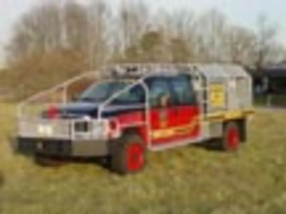 Exterior view of small fire truck showing cab, body compartments, and wheel/tire area.