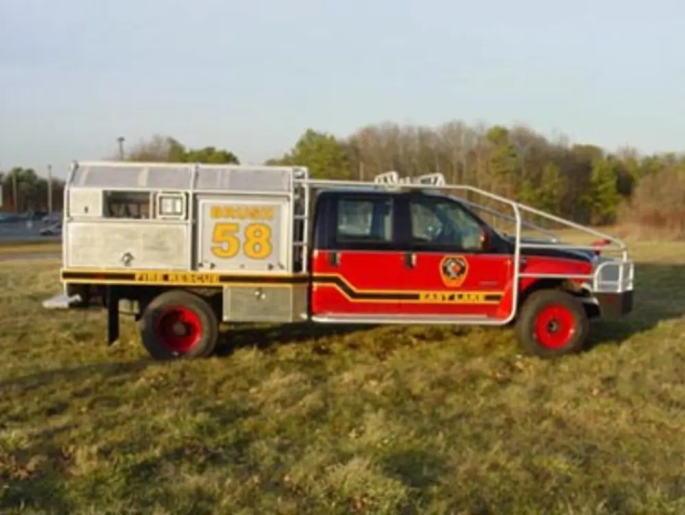 Exterior view of small fire truck showing cab, body compartments, and wheel/tire area.