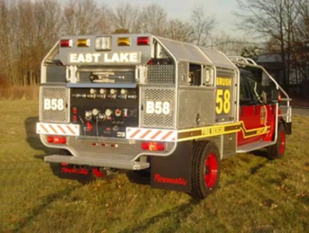 Exterior view of small fire truck showing cab, body compartments, and wheel/tire area.