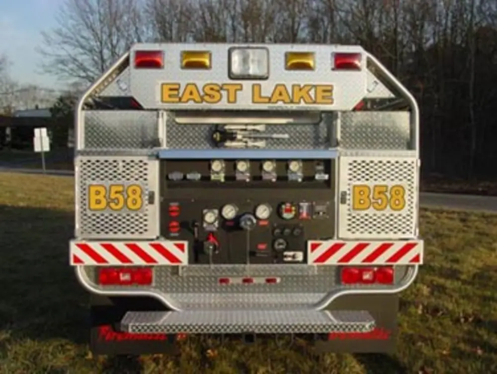 Exterior view of small fire truck showing cab, body compartments, and wheel/tire area.