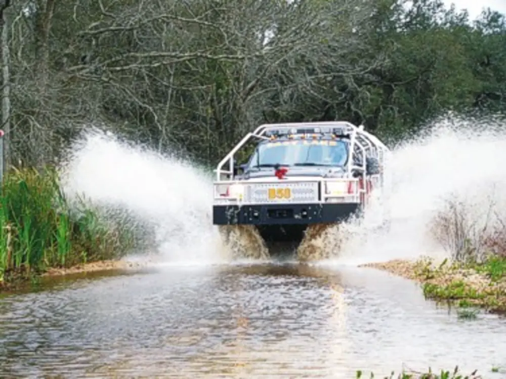 Exterior view of small fire truck showing cab, body compartments, and wheel/tire area.
