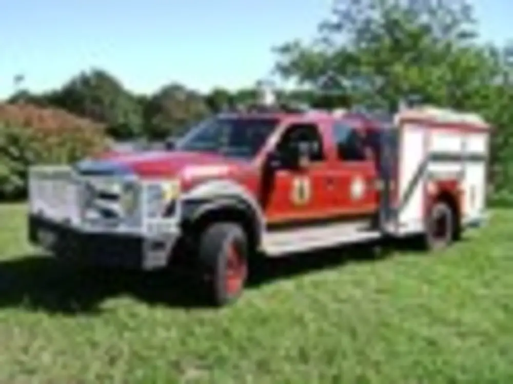 Exterior view of small fire truck showing cab, body compartments, and wheel/tire area.