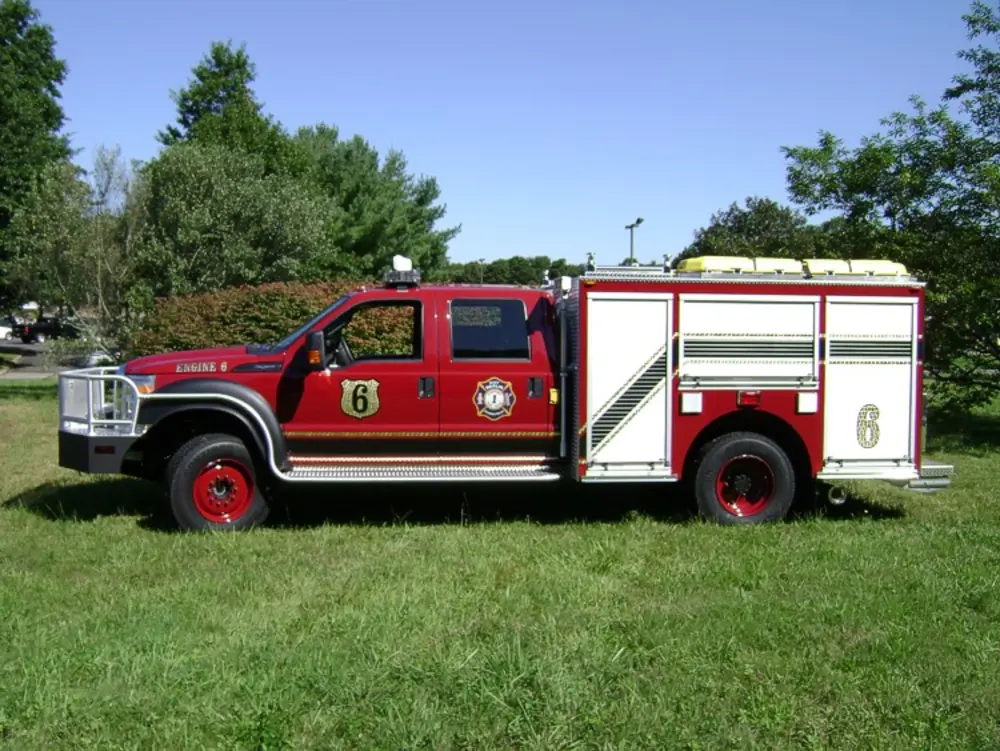 Exterior view of small fire truck showing cab, body compartments, and wheel/tire area.