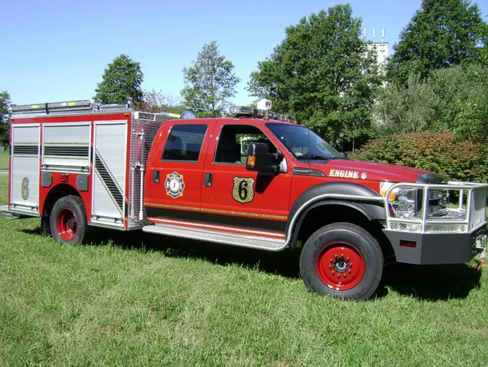 Exterior view of small fire truck showing cab, body compartments, and wheel/tire area.