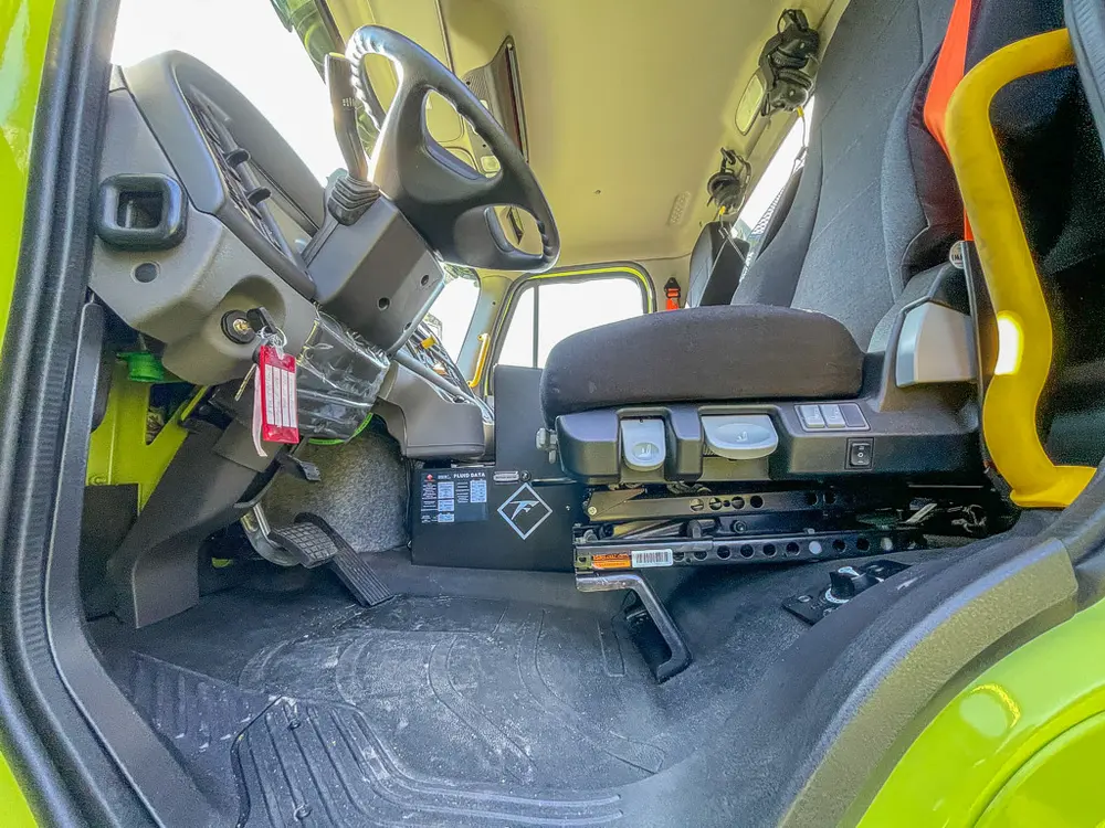 Driver seat base and side controls near open door.