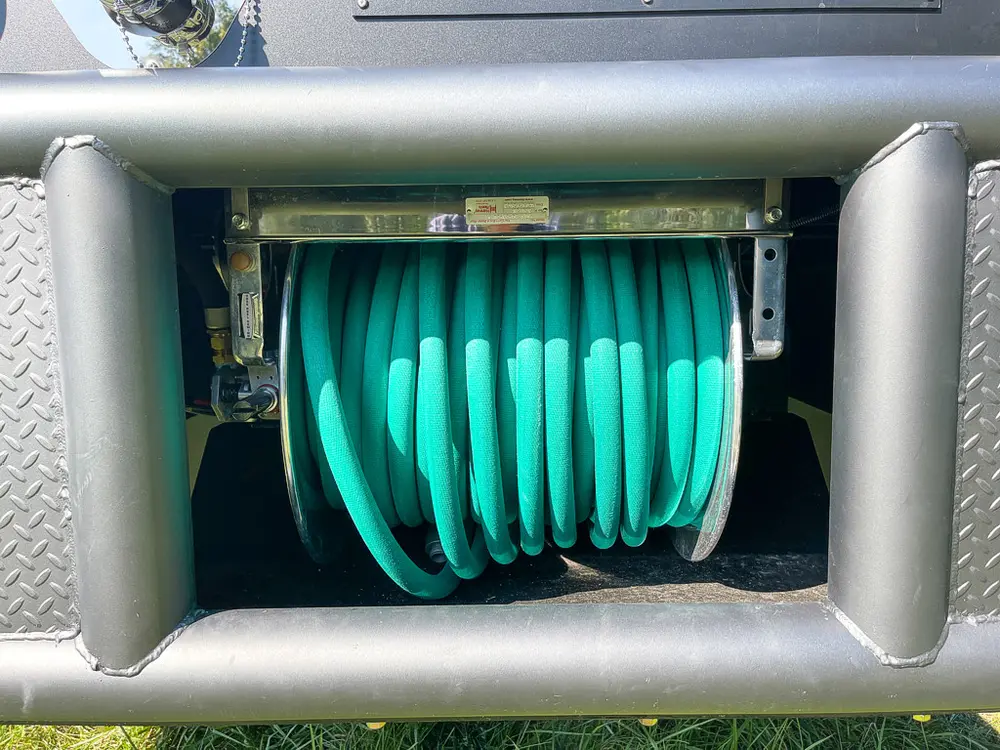 Recessed hose reel compartment with green hose coiled inside.