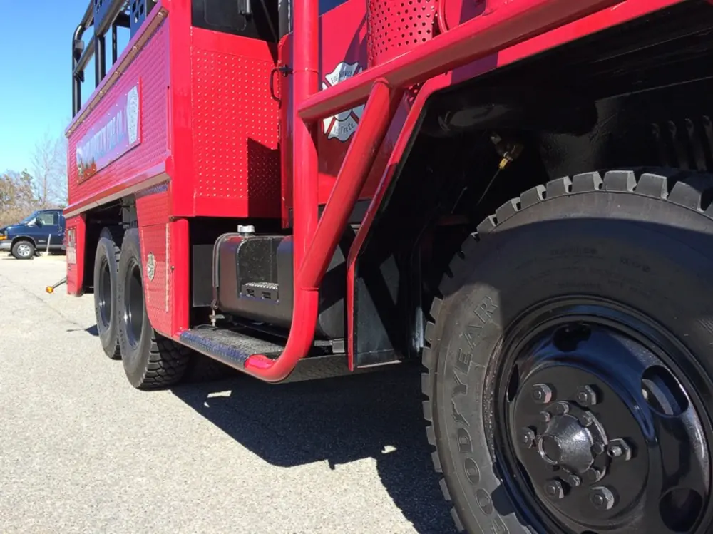 Exterior view of small fire truck showing cab, body compartments, and wheel/tire area.