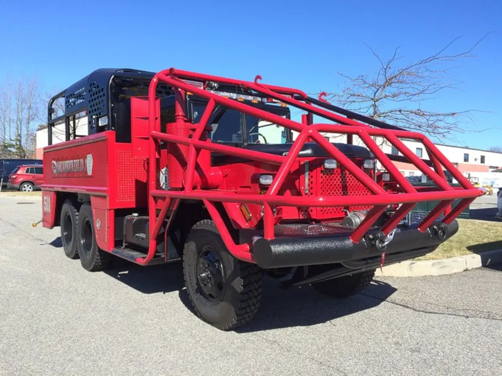 Exterior view of small fire truck showing cab, body compartments, and wheel/tire area.