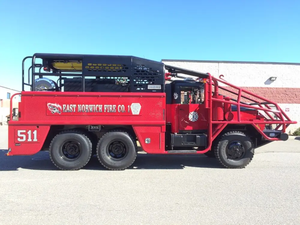 Exterior view of small fire truck showing cab, body compartments, and wheel/tire area.