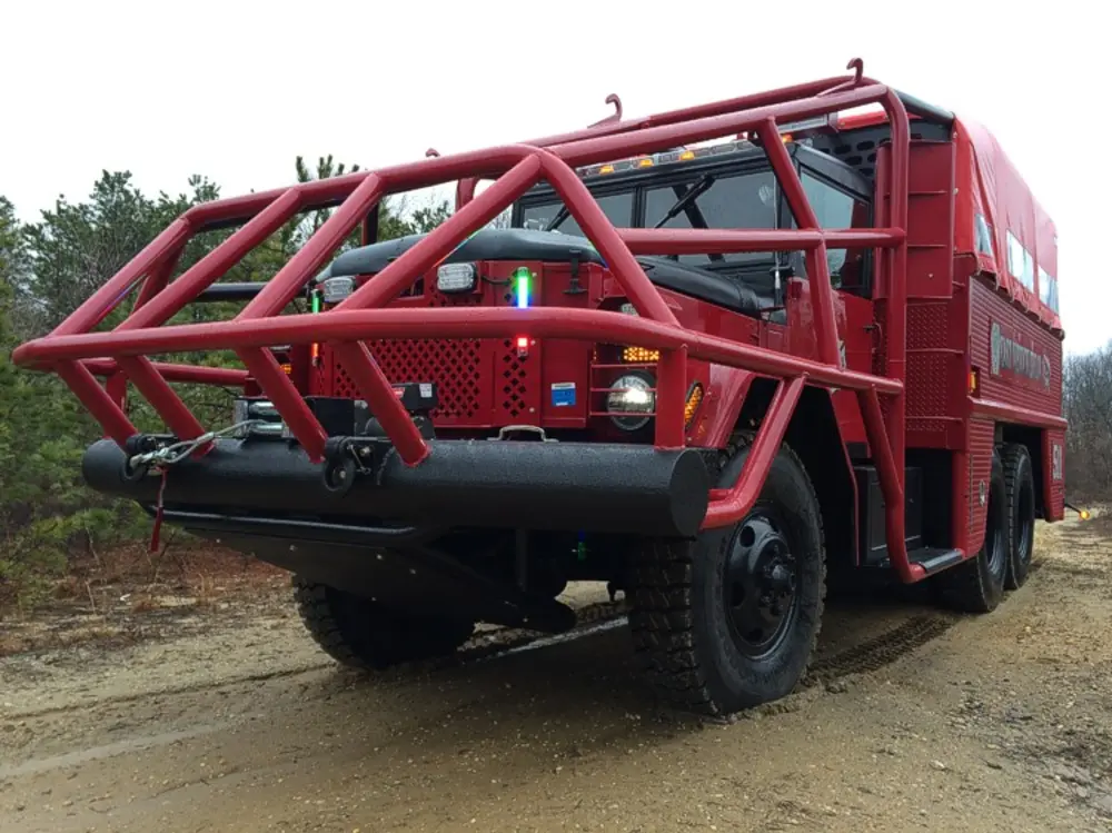 Exterior view of small fire truck showing cab, body compartments, and wheel/tire area.