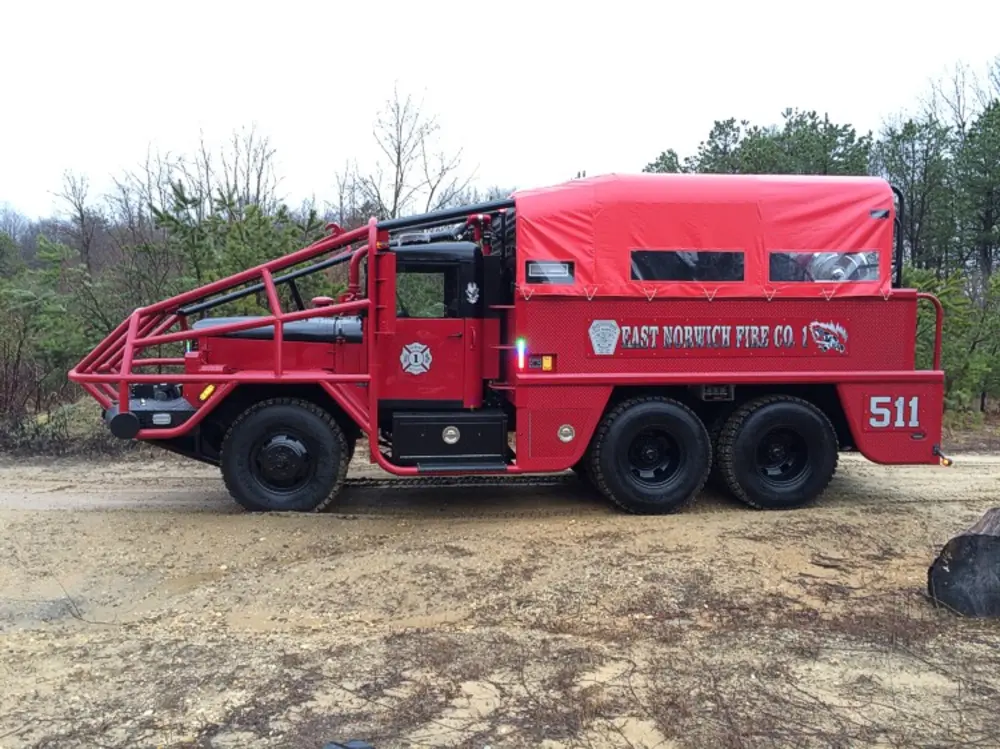 Exterior view of small fire truck showing cab, body compartments, and wheel/tire area.