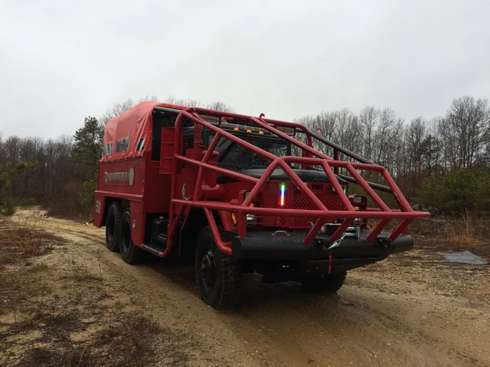 Exterior view of small fire truck showing cab, body compartments, and wheel/tire area.