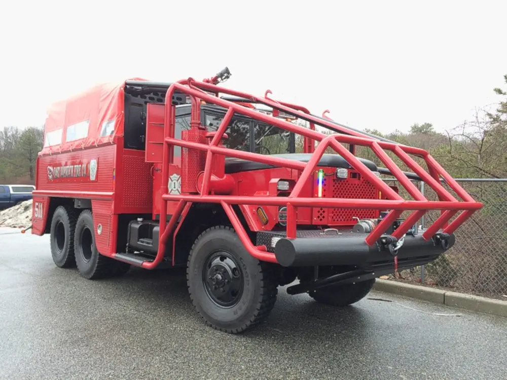 Exterior view of small fire truck showing cab, body compartments, and wheel/tire area.