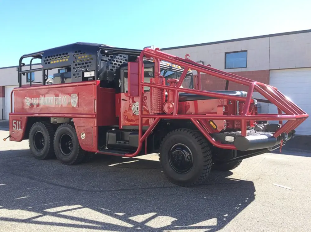 Exterior view of small fire truck showing cab, body compartments, and wheel/tire area.