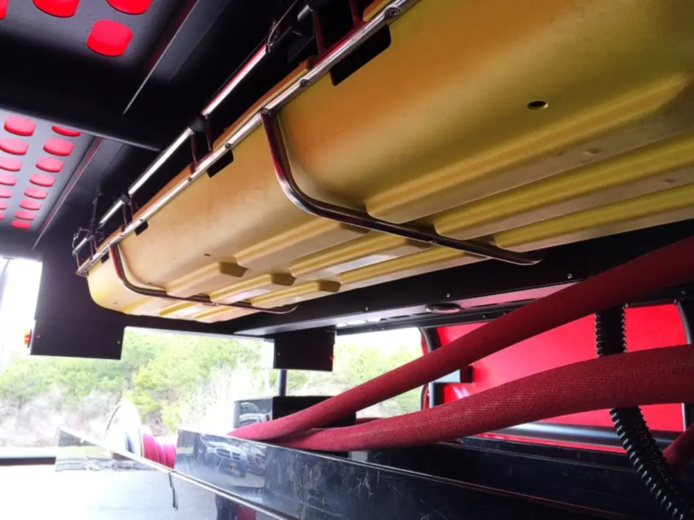Exterior view of small fire truck showing cab, body compartments, and wheel/tire area.