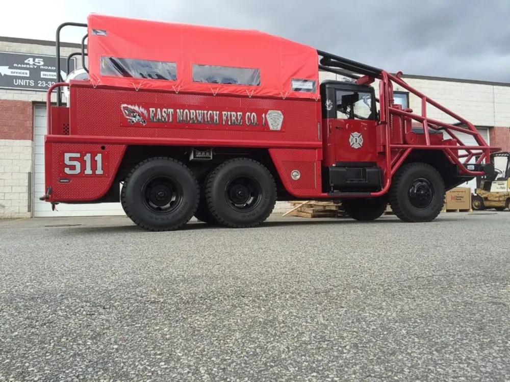 Exterior view of small fire truck showing cab, body compartments, and wheel/tire area.