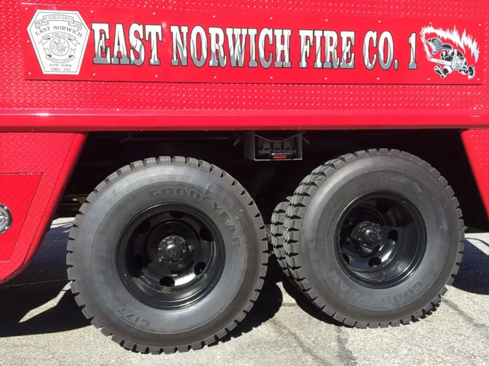 Exterior view of small fire truck showing cab, body compartments, and wheel/tire area.