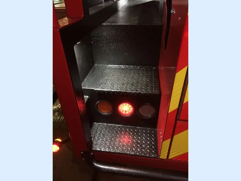 Exterior view of small fire truck showing cab, body compartments, and wheel/tire area.