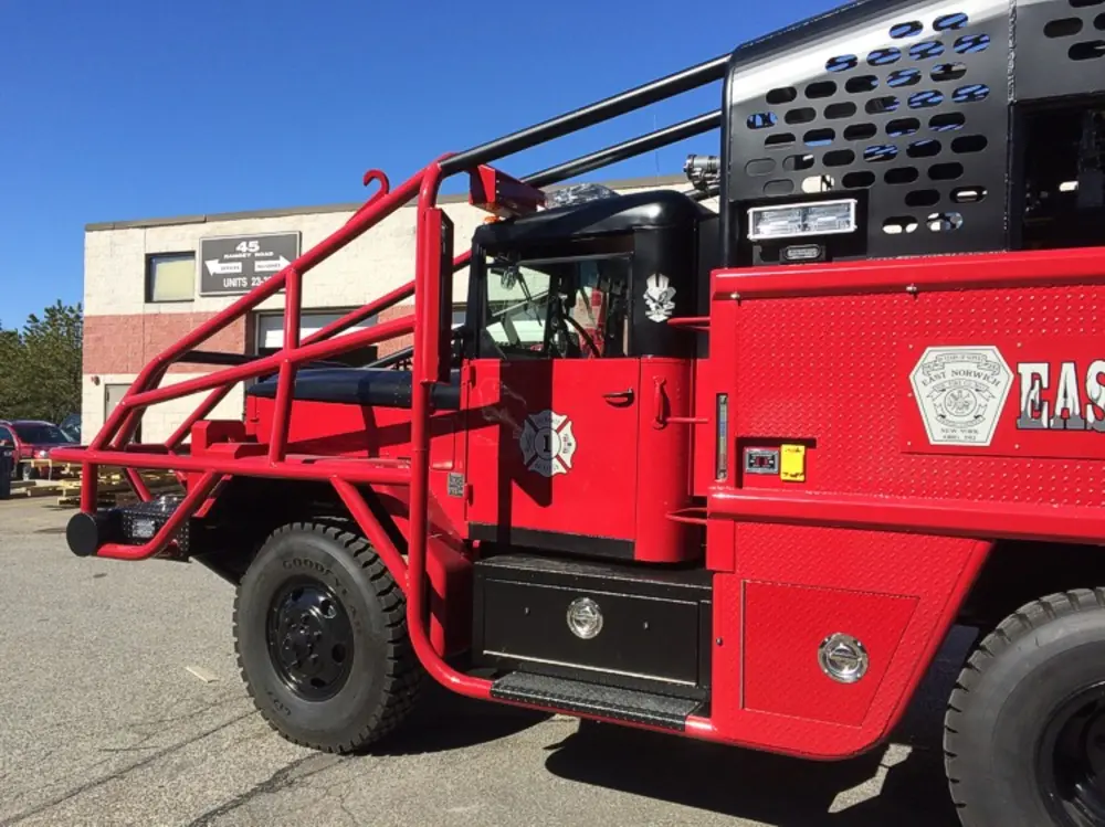 Exterior view of small fire truck showing cab, body compartments, and wheel/tire area.