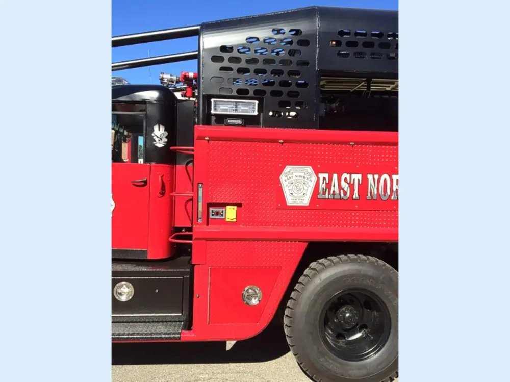 Exterior view of small fire truck showing cab, body compartments, and wheel/tire area.