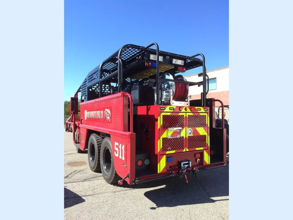 Exterior view of small fire truck showing cab, body compartments, and wheel/tire area.
